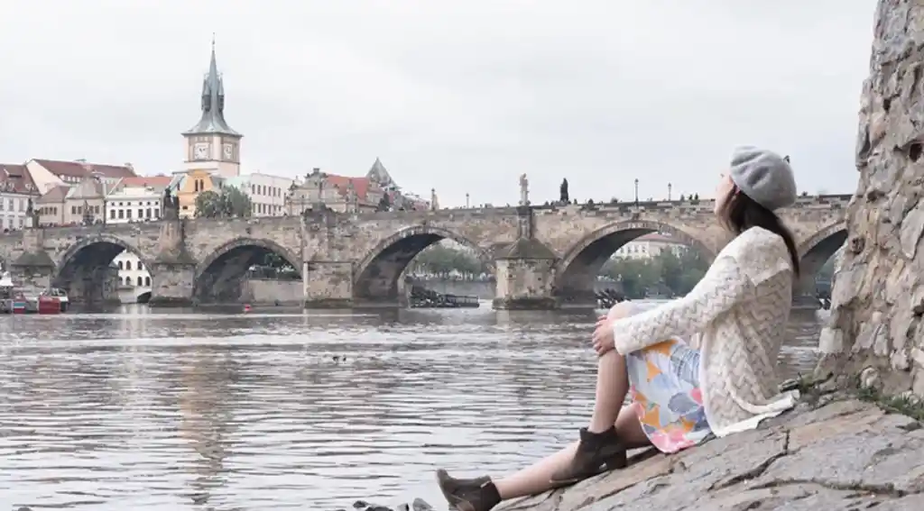 woman sitting next to charles bridge in prague